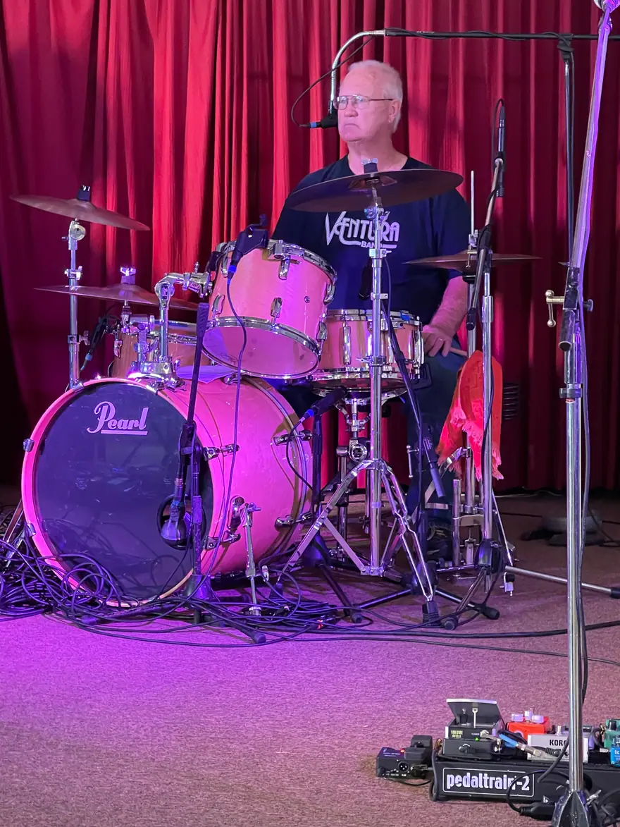 Ventura Band drummer in a black shirt playing a pink Pearl drum kit in front of a red curtain