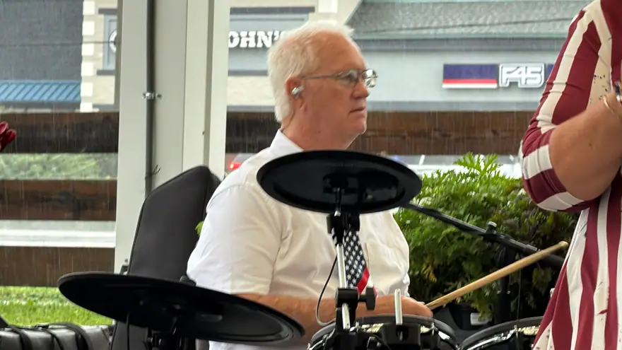 Ventura Band drummer in a white shirt and sunglasses playing a drum kit under a white tent