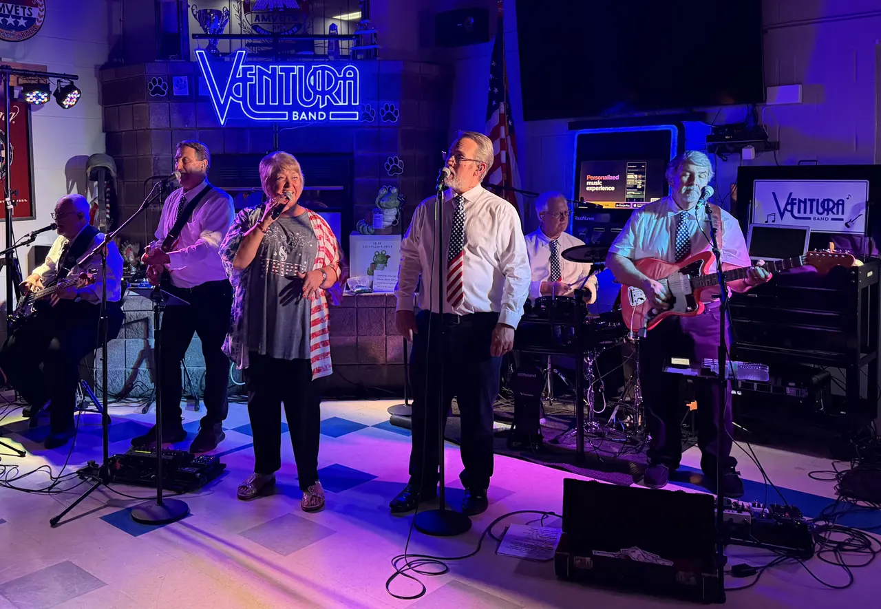 Two Ventura Band vocalists singing under the lit Ventura Band sign