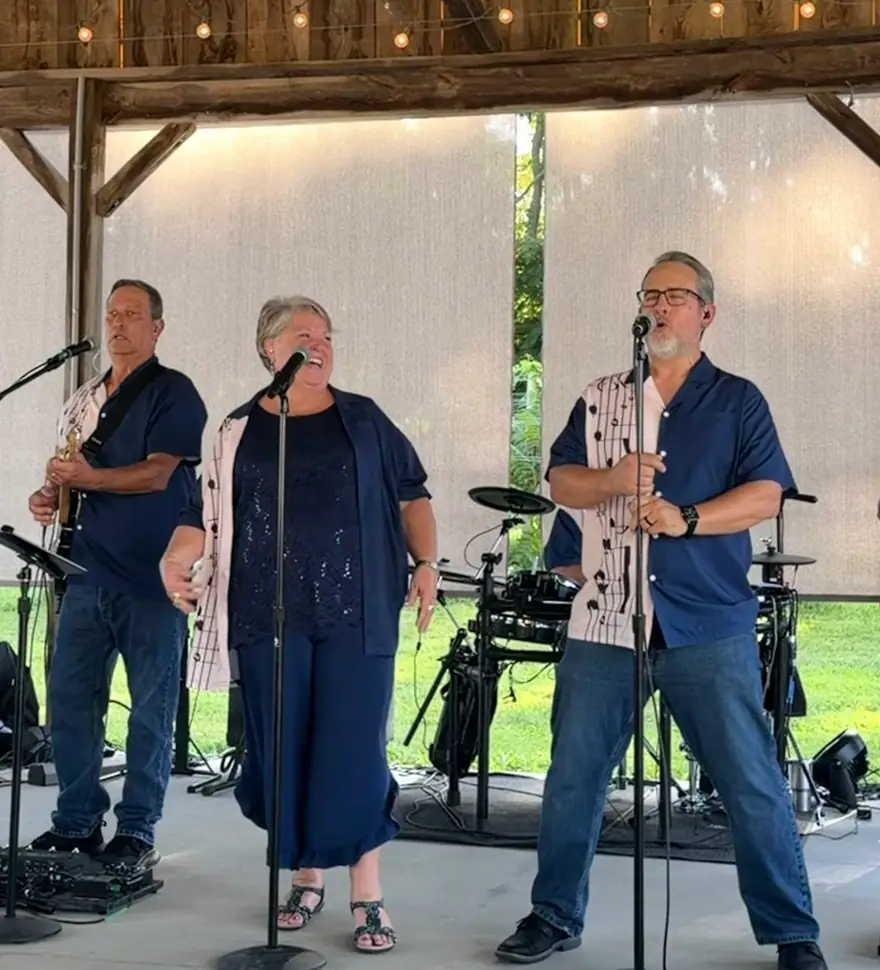 Three Ventura Band singers in navy music-note shirts performing under a barn pavilion